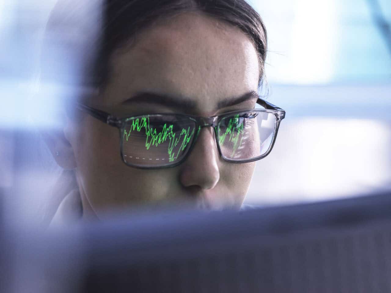 Eine junge Frau betrachtet einen Börsenkurs am Monitor und überlegt, welche Ordertypen sie nutzen möchte.
