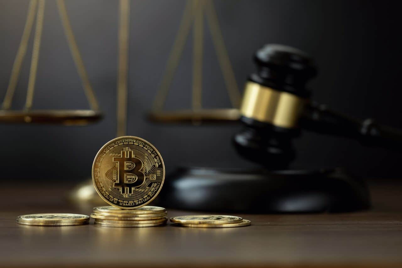 Ein Stapel Bitcoin-Münzen vor einem Richterhammer symbolisiert die Krypto-Steuer.