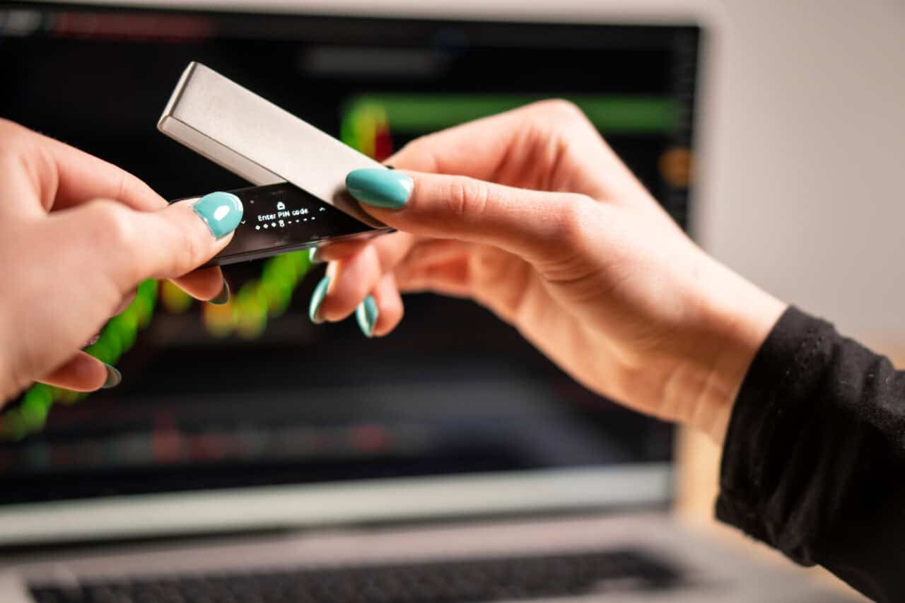 Das Bild zeigt, wie der Ledger Nano X zum Einrichten vor einem Laptop in der Luft gehalten wird.