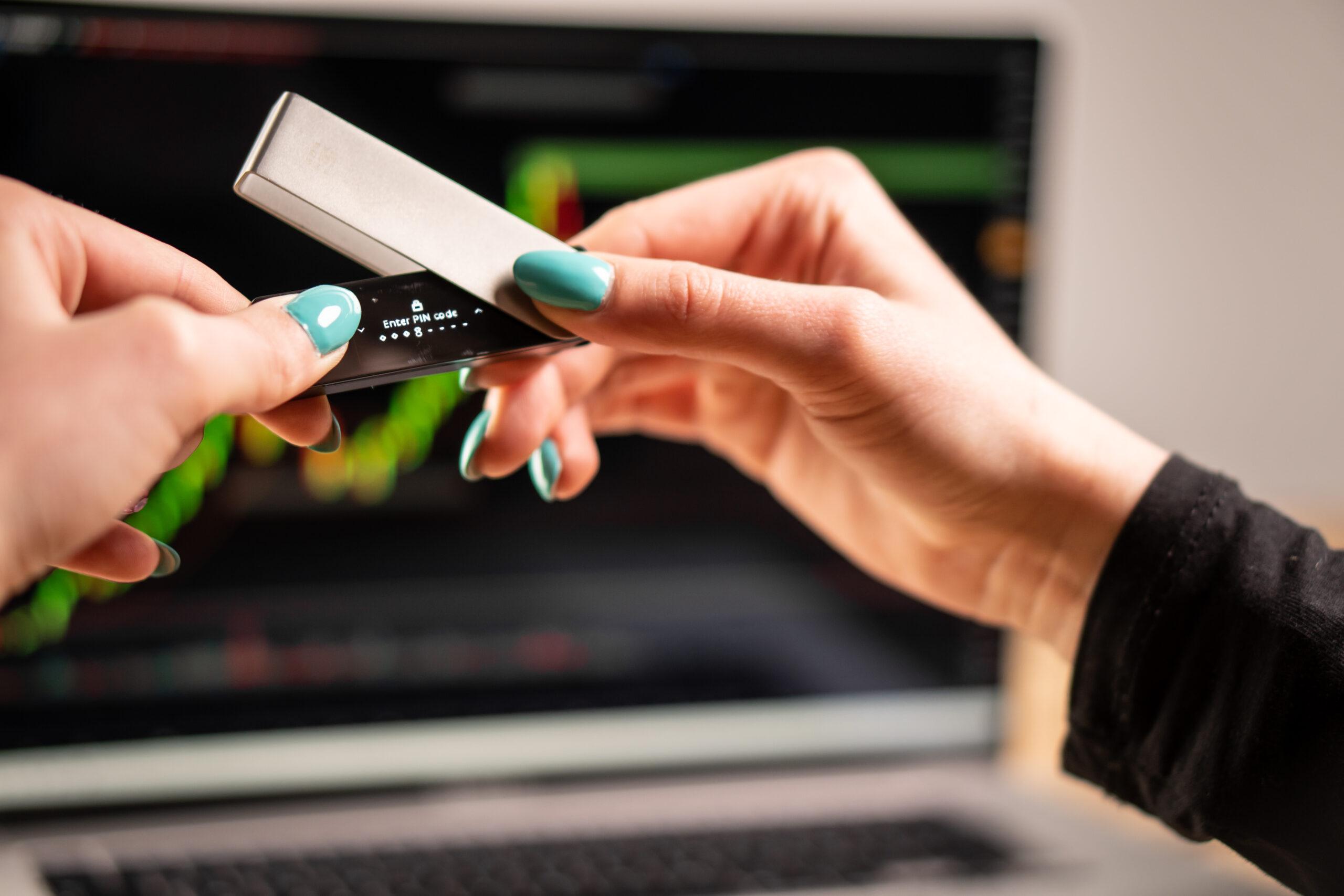 Das Bild zeigt, wie der Ledger Nano X zum Einrichten vor einem Laptop in der Luft gehalten wird.