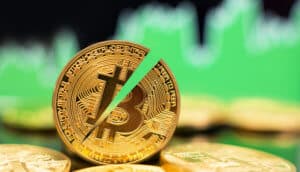 halbierte bitcoin münze die zwischen liegenden bitcoin münzen steht, im Hintergrund grüne Charts als Symbol für einen Bitcoin-Kurs-Anstieg nach dem Halving