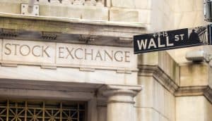 Vor der Steinfassade der New Yorker Börse ist ein Straßenschild der Wall Street angebracht, das die Überschneidung von traditionellem Finanzwesen und modernen Vermögenswerten wie Bitcoin hervorhebt.