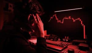 Trader sitzt vor einem Computer mit roten Candlestick-Charts und hält den Kopf in den Händen. Symbolbild für Krypto-Liquidationen, Marktcrash und Leverage-Verluste.