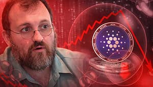 Porträt eines bärtigen Mannes mit Brille im Vordergrund, links im Bild. Rechts daneben eine schwebende Cardano-Münze (ADA) in einer transparenten Blase über gestapelten Coins. Im Hintergrund zeigt eine rote Grafik einen stark fallenden Cardano-Kurs vor einer dunkelroten, digitalen Markt-Visualisierung.