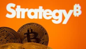 Strategy-Logo, auf orangenem Hintergrund, davor Bitcoin-Münzen