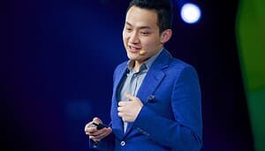 Justin Sun ist elegant in einen blauen Anzug gekleidet, spricht selbstbewusst in ein Headset-Mikrofon und leitet das Publikum auf der schwach beleuchteten Bühne nahtlos mit seinem Klicker an.