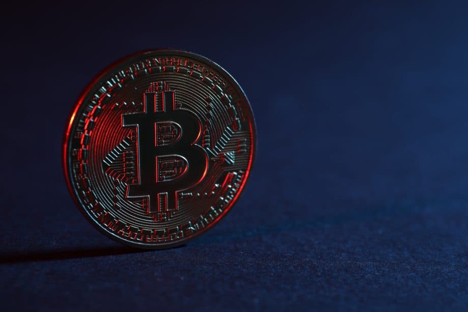 Bitcoin-Münze schimmert rötlich vor einem dunkelblauen Hintergrund.