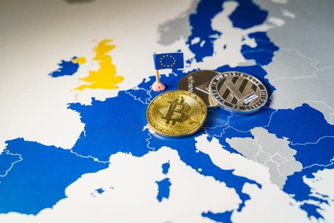 Man sieht die Karte Europas mit Hervorhebung der EU-Länder. Auf der Karte liegt eine Bitcoin-Münze und zwei andere Krypto-Coin-Münzen ab.