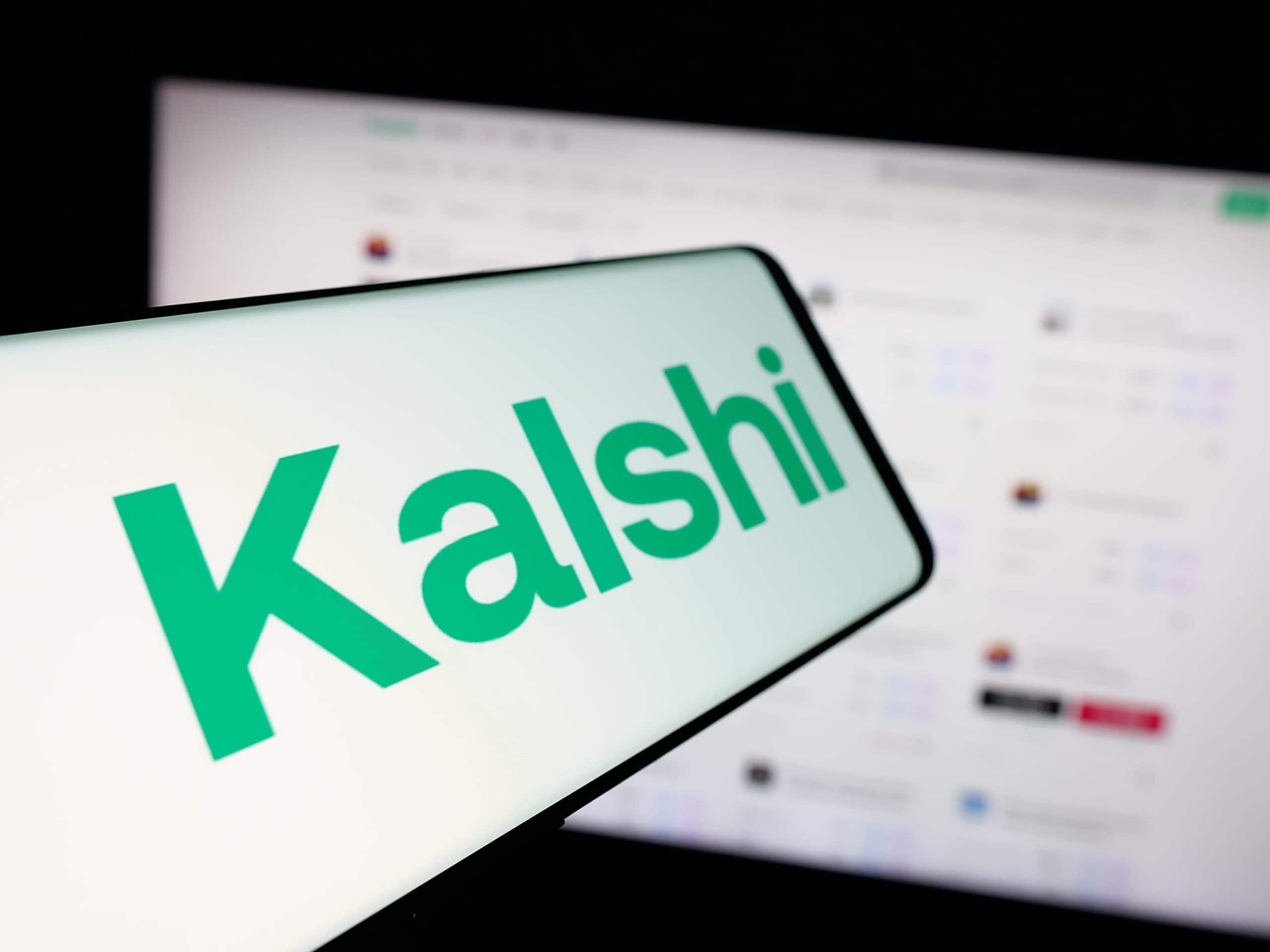 Kalshi-Logo auf einem Smartphone vor einem Computerbildschirm.