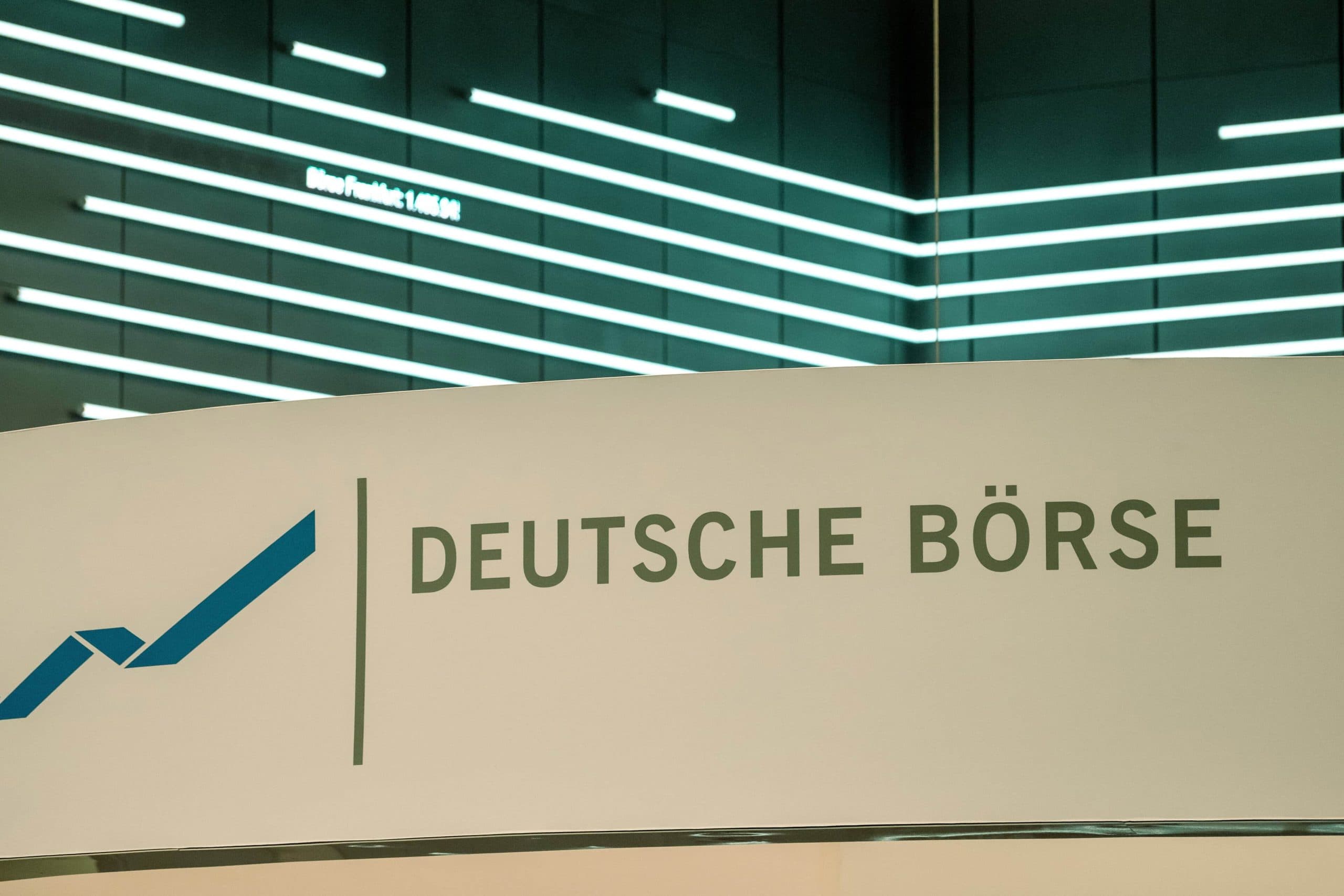 Ein Schild mit dem Logo und dem Namen der Deutschen Börse vor einer modernen, beleuchteten Wand mit horizontalen Lichtbändern unterstreicht den Fokus auf Innovation und Integration, einschließlich der Entwicklungen bei Stablecoins.