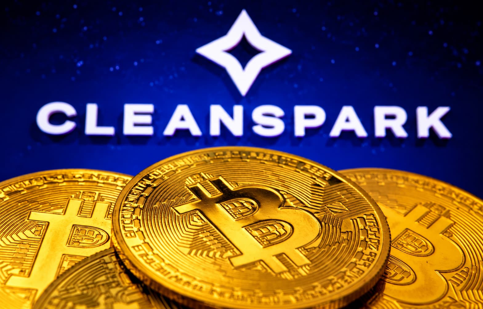 CleanSpark Logo mit weißem Stern-Symbol und Schriftzug vor einer dunkelblauen Wand mit Sternenmuster