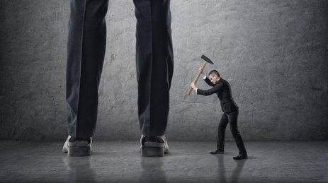 Small businessman hitting giant legs of another with hammer