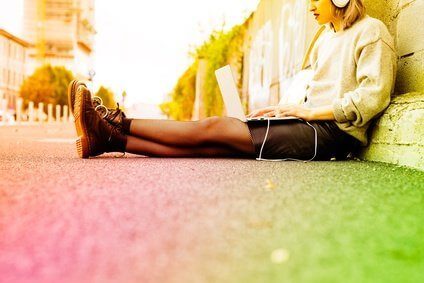 Young beautiful caucasian purple grey hair woman outdoor in the city sitting on the floor listening music with head phones and computer leaning on her knee - technology, music, social network concept