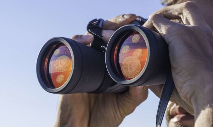 Ein Mensch blickt mit einem Fernglas in die Ferne, auf den Gläsern sieht man Bitcoin Münzen