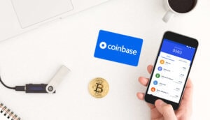 Man sieht ein Smartphone mit der Coinbase App, eine Bitcoin-Münze sowie ein HArdware Wallet auf einem Tisch liegen.