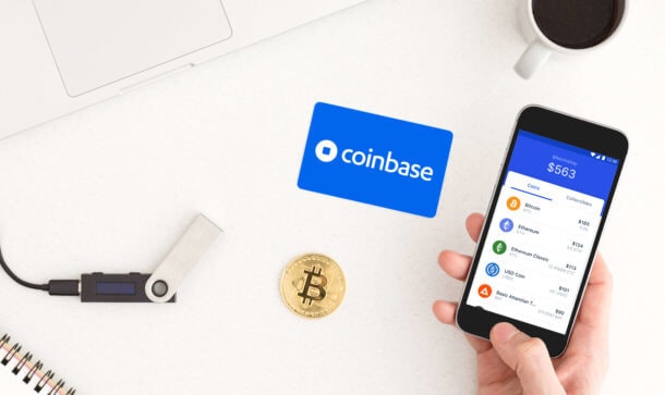 Coinbase überlegt 18 neue Kryptowährungen zu listen Man sieht ein Smartphone mit der Coinbase App, eine Bitcoin-Münze sowie ein HArdware Wallet auf einem Tisch liegen.