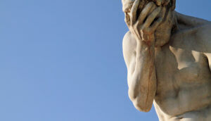 Eine Statur aus Stein verdeckt sich mit Hand das Gesicht.