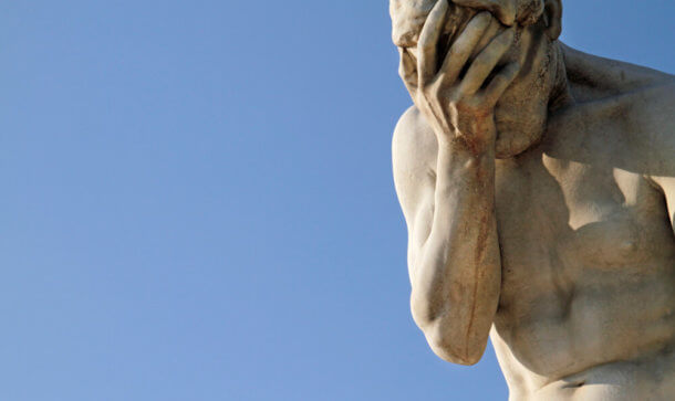 Eine Statur aus Stein verdeckt sich mit Hand das Gesicht.