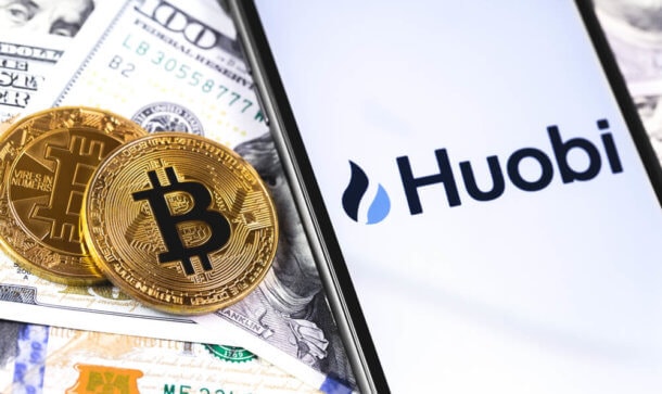 Huobi: Erster Exchange Token mit japanischem Siegel Auf einem Smartphone steht Huobi geschrieben und man sieht Geldscheine sowie Bitcoin-Münzen im Hintergrund.