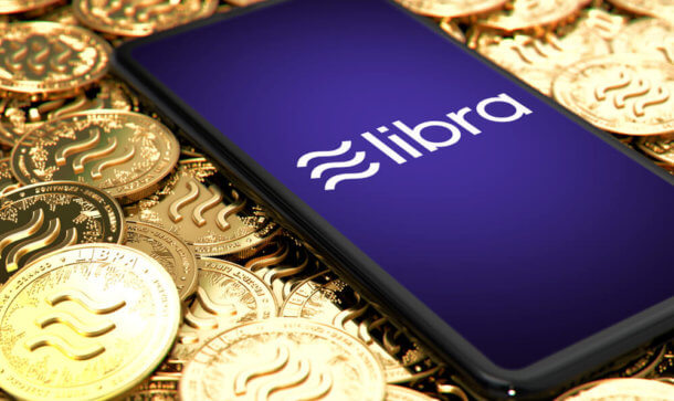 Facebook auf Erfolgskurs: Libra Association gibt neue Mitglieder bekannt Libra-Logo auf Smartphone, das auf Goldmünzen mit Libra-Logo liegt