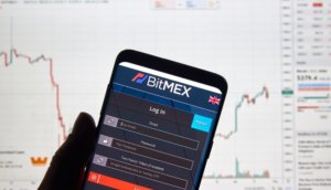 Smartphone mit App von BitMEX vor Desktop-Hintergrund mit Chart.