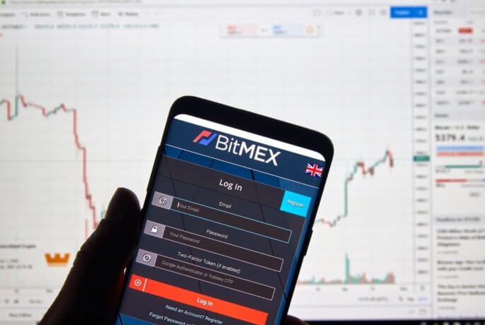 Smartphone mit App von BitMEX vor Desktop-Hintergrund mit Chart.