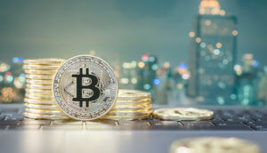 Eine aufgerichtete Bitcoin-Münze steht vor einem Stapel Bitcoin-Münzen, die vor einer Skyline liegend