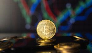 Bitcoin-Münze steht aufgerichtet auf einem Stapel Bitcoin-Münzen vor einer Chart.