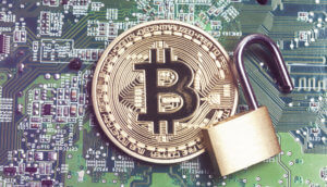 Eine Bitcoin-Münze auf einer Platine, daneben ein geöffnetes Schloss.