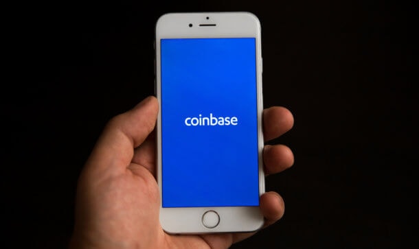 Sicherheit für den DeFi-Markt: Coinbase entwickelt Preis Feed hand hält ein smartphone, auf dem das coinbase-logo zu sehen ist
