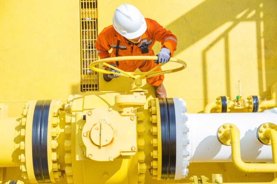 Wie der Ölpreiskollaps (WTI) die Notwendigkeit digitaler Assets offenbart Arbeiter befindet sich auf gelber Bohrinsel für Öl und dreht an einem Ventil.