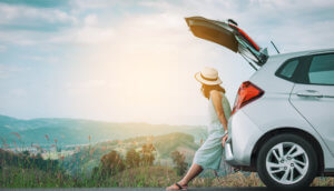 frau mit hut lehnt an einem auto vor einem bergpanorama