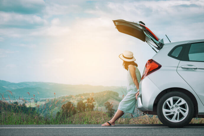 frau mit hut lehnt an einem auto vor einem bergpanorama