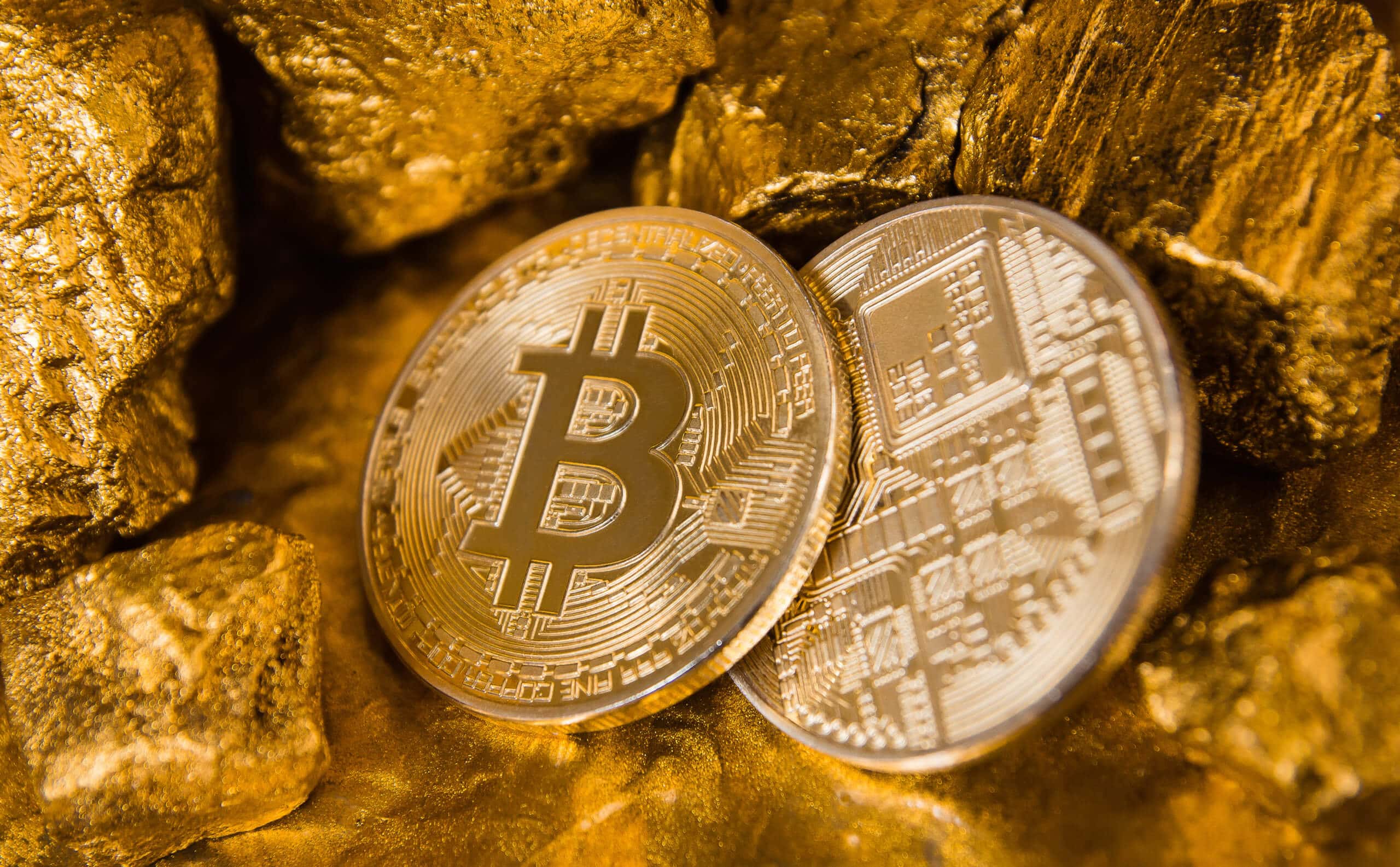 Zwei Bitcoin Münzen, eine von vorne, die andere von hinten, inmitten von einigen Goldnuggets, symbol für potential des Bitcoin-Kurs