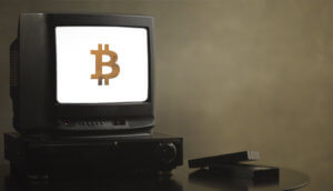 bitcoin symbol auf einem weißen bildschirm eines alten fernsehers vor einer dunklen wand