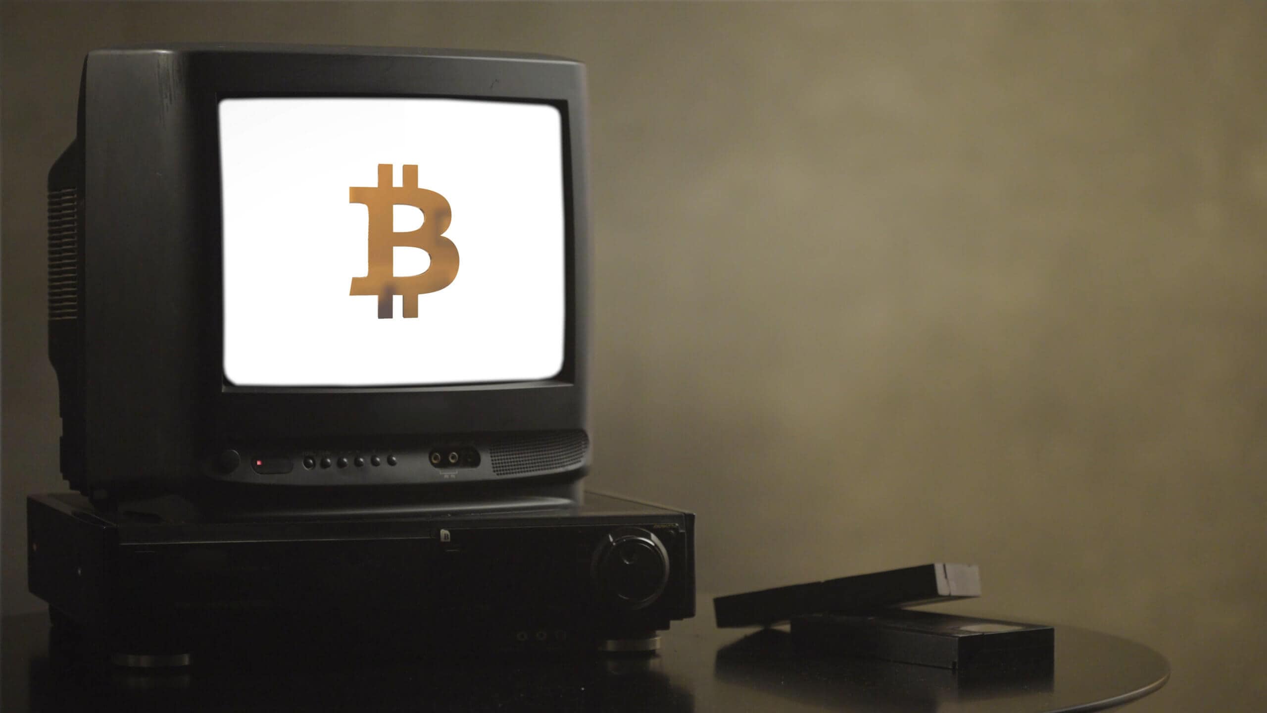 bitcoin symbol auf einem weißen bildschirm eines alten fernsehers vor einer dunklen wand