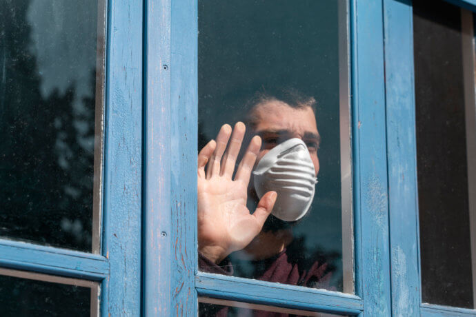 Sehnsuchtsvoll aus dem Fenster blickender Mann mit Mundschutz