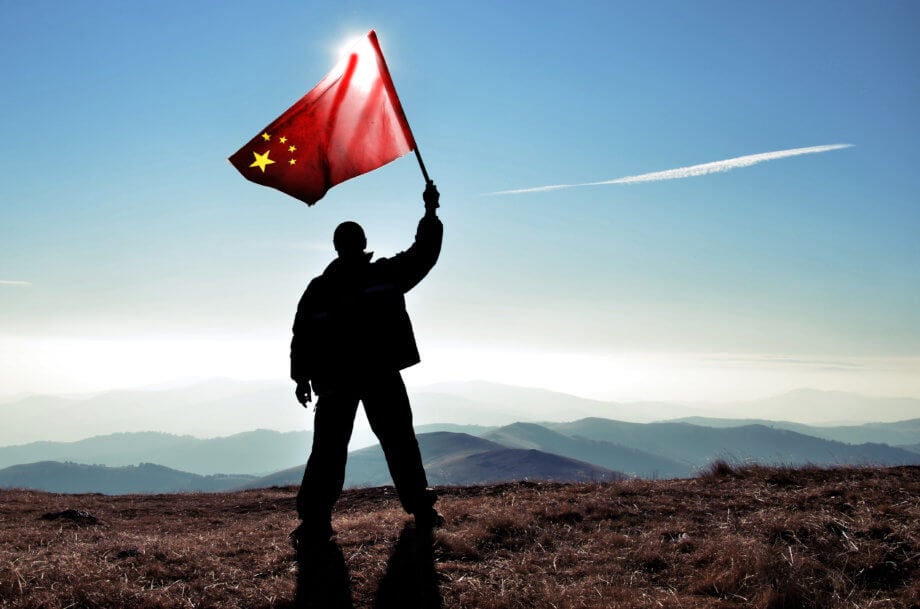 Nun ist es offiziell: China führt westliches Geldsystem mit CBDC vor Mann steht auf Berg und hält chinesische Flagge hoch als Zeichen für den Start von CBDC