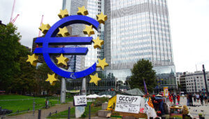 Eurozeichen im Vordergrund und im Hintergrund ein Frankfurter Bankgebäude