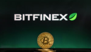 In der Mitte steht eine goldene Bitcoin Münze und im Hintergrund wird die Bitfinex Börse angezeigt