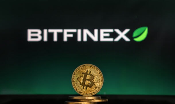 Reich hodln: Bitfinex führt Staking Rewards ein In der Mitte steht eine goldene Bitcoin Münze und im Hintergrund wird die Bitfinex Börse angezeigt