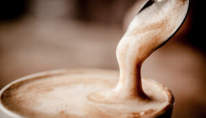 Löffel mit Milchschaum über einer Tasse