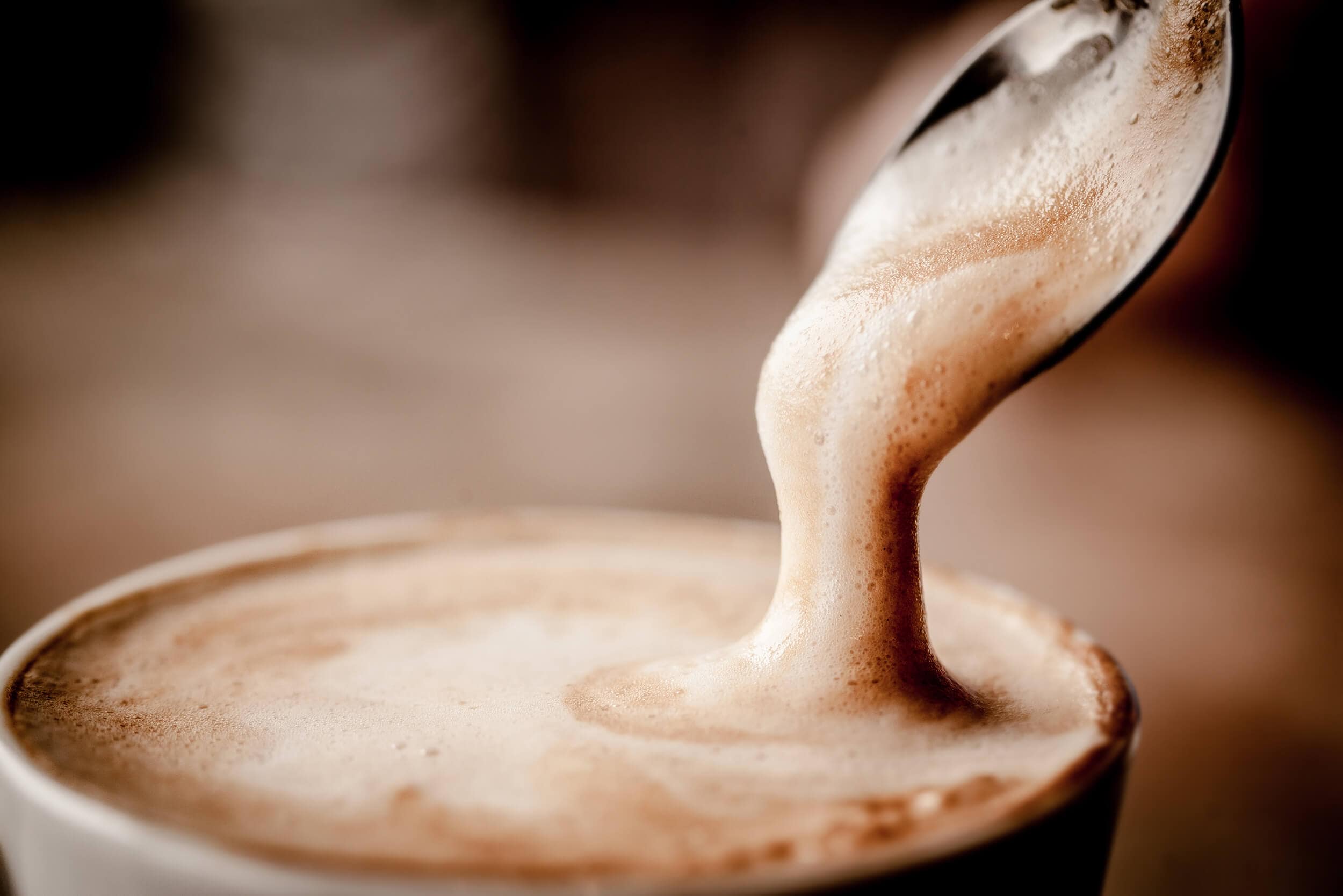 Löffel mit Milchschaum über einer Tasse