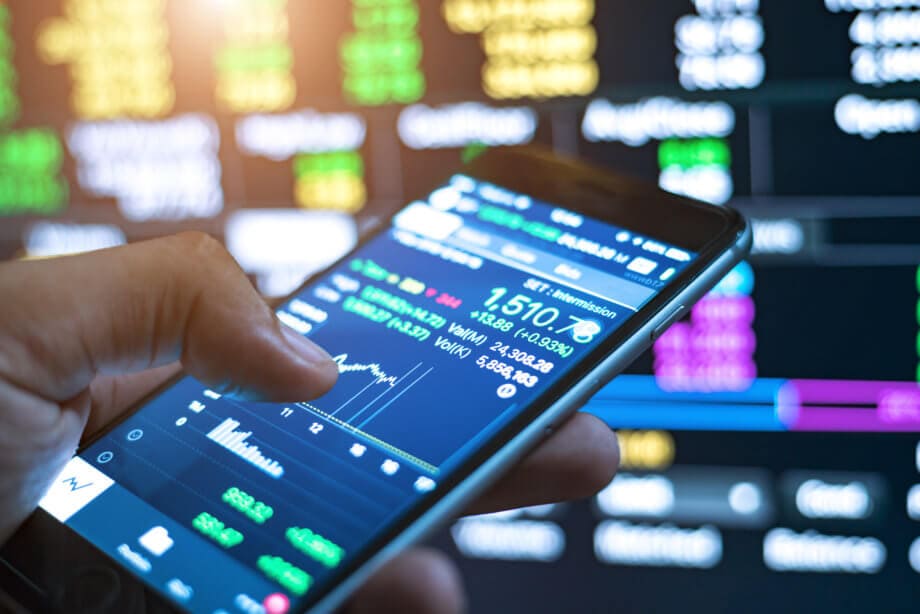 Blockchain-Assets: USA bekommen neues Trading-Netzwerk smartphone mit daumen zeigt charts im hintergrund börse