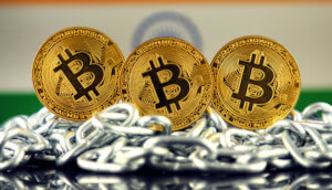 Drei Bitcoin-Münzen auf einer Kette, im Hintergrund die indische Flagge