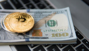 Ein paar Bitcoin-Münzen auf einem Haufen Dollar-Scheine auf einem Laptop.