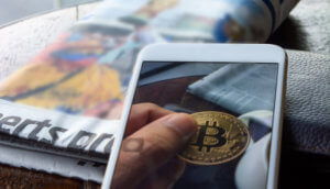 Bitcoin auf Iphone mit Tageszeitung daneben