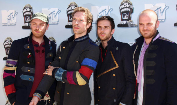 Zumo: Coldplay Bassist unterstützt Bitcoin App Die Bandmitglieder von Coldplay stehen vor einer Plakatwand für Fotoshooting.