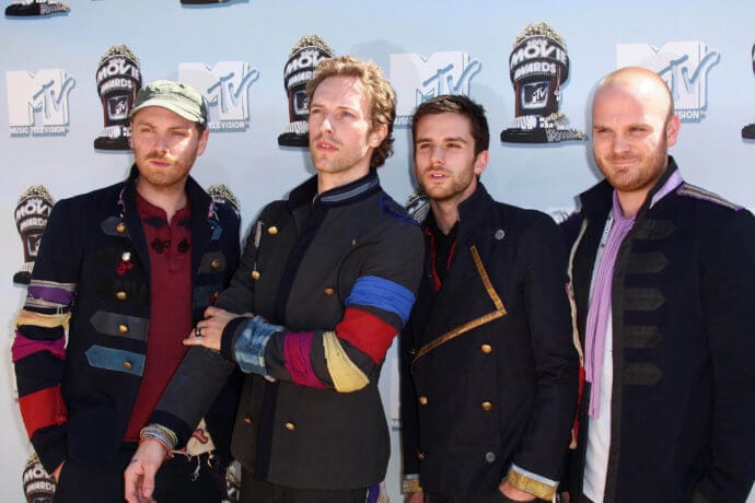 Die Bandmitglieder von Coldplay stehen vor einer Plakatwand für Fotoshooting.