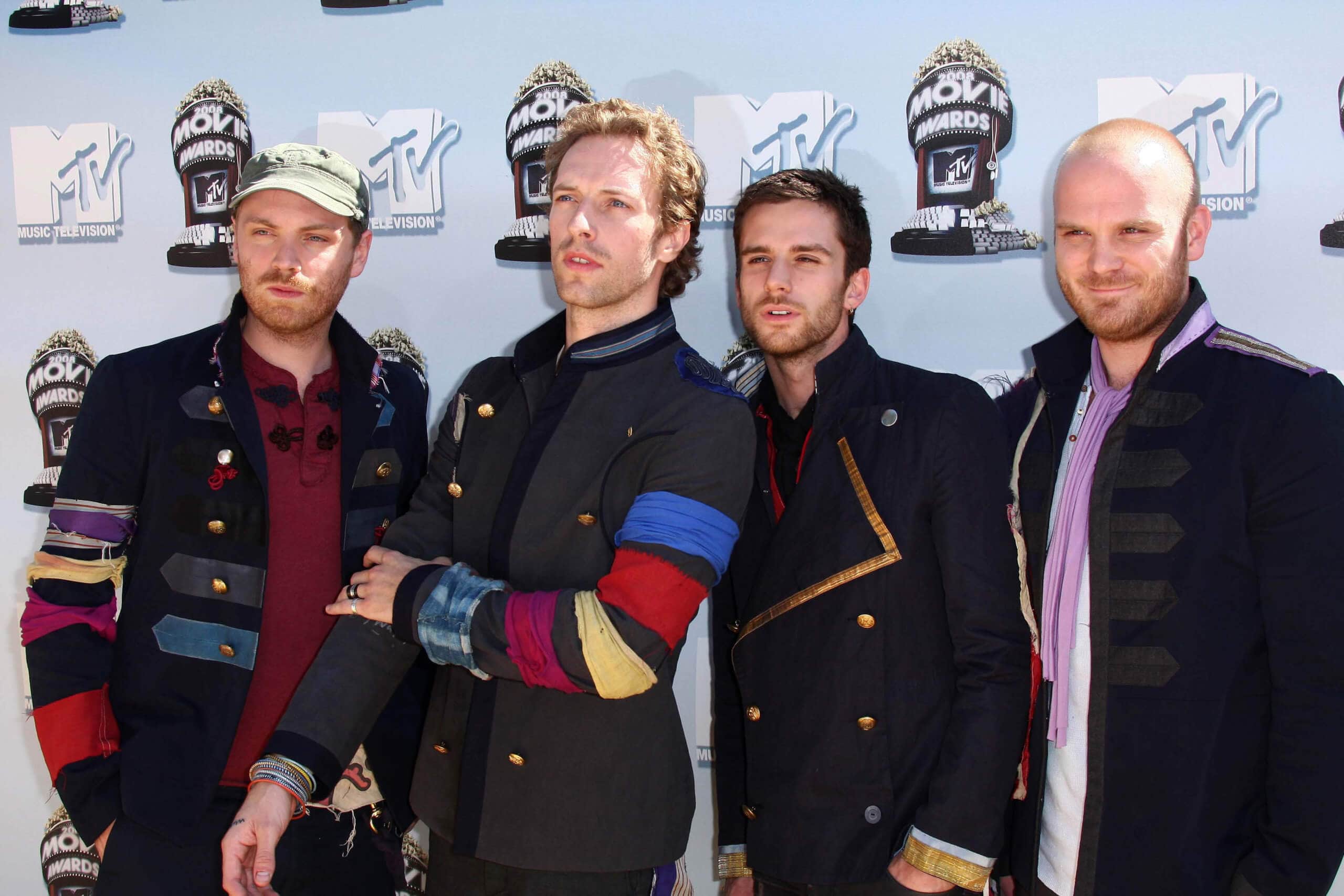 Die Bandmitglieder von Coldplay stehen vor einer Plakatwand für Fotoshooting.